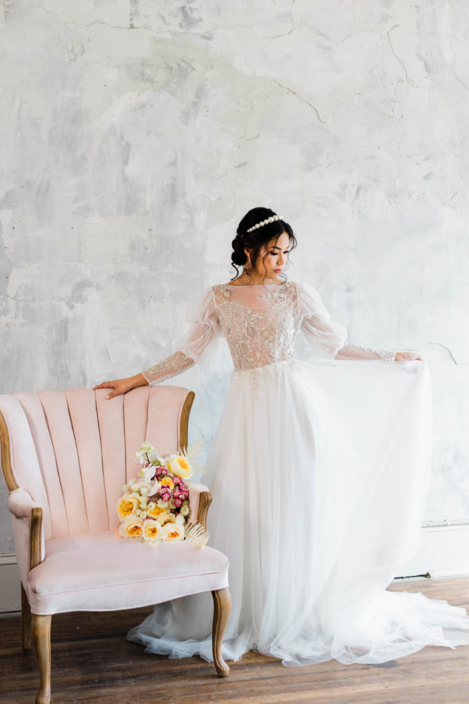 Beautiful fine art bridal portrait of bride holding the train of her dress next to pink chair. Taken by Captured By Lau Photography, a St. Augustine, Florida Wedding Photographer.