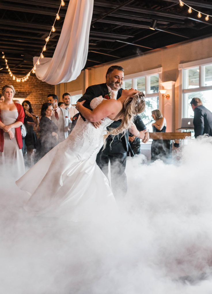 Groom dips the bride on the reception dance floor surrounded by a cloud of smoke at their wedding at the The White Room in St. Augustine, Florida. Photography by Captured By Lau Photography, a St. Augustine, Florida Wedding Photographer.