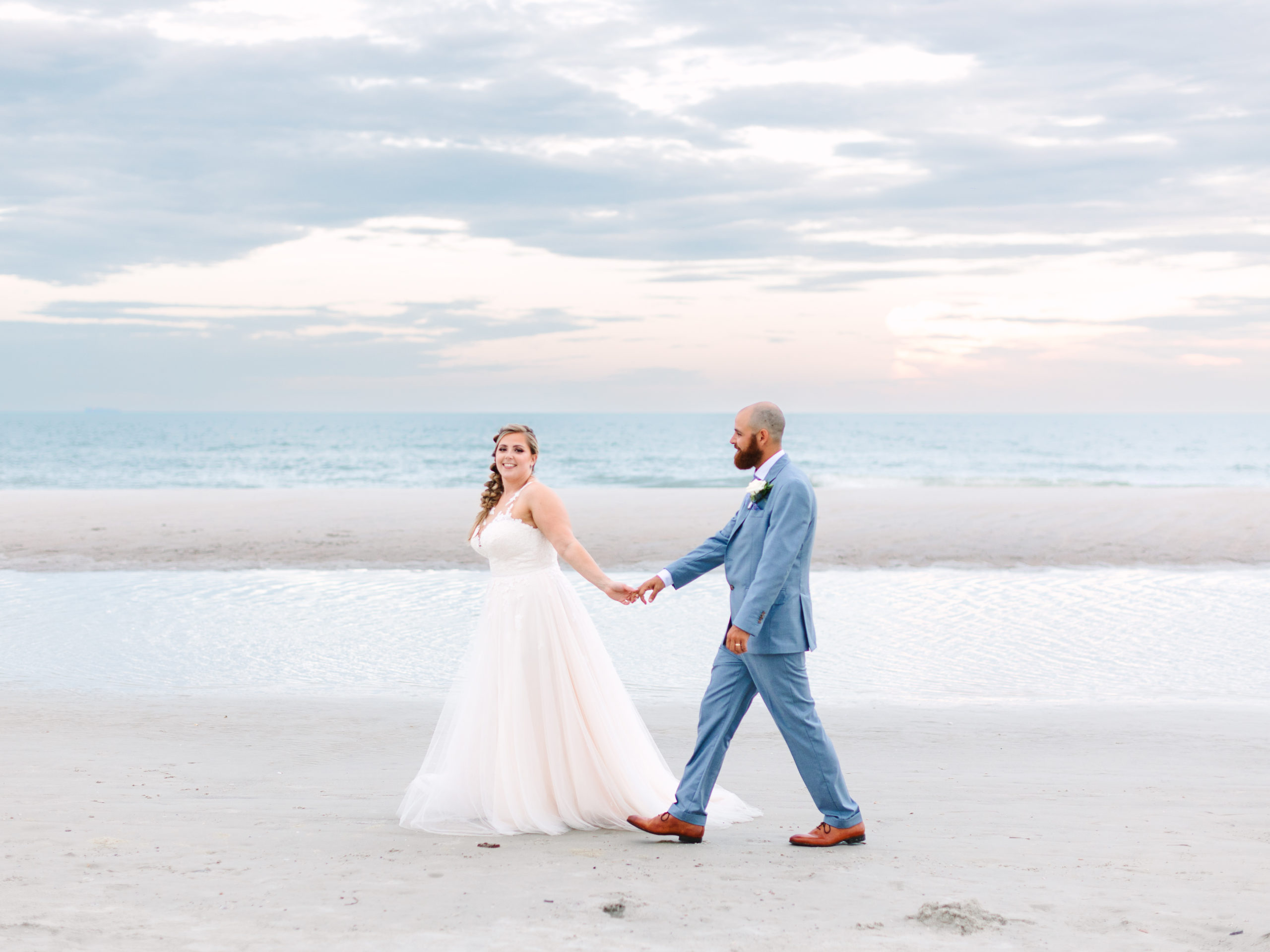 Bride and groom holding hands on the beach at One Ocean Resort in Atlantic Beach captured by Laura Perez Photography.