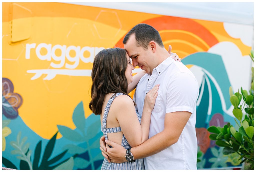 A newly engaged couple embrace in front of a colorful sign during a session by Laura Perez Photography. 