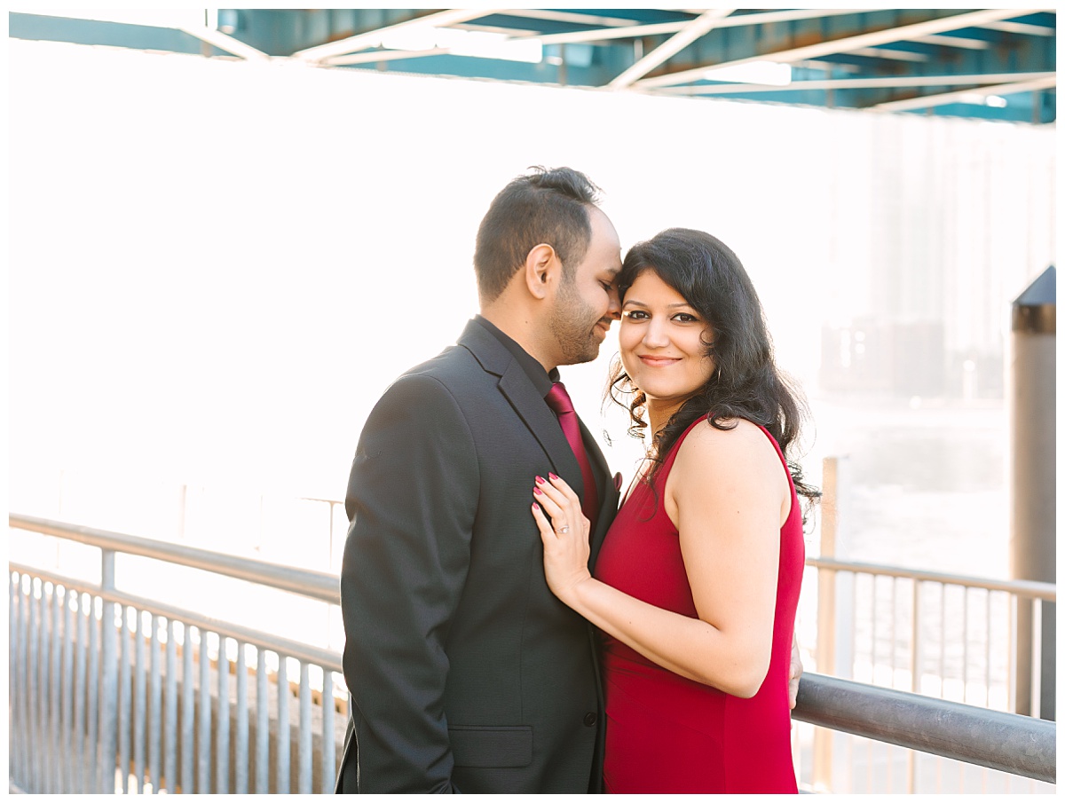 A dark haired couple in formal attire pose next to the water for their engagement session in downtown Jacksonville, Florida.