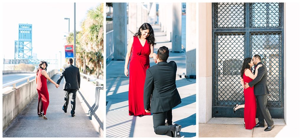 A man in a black suit kneels in front of a woman in a floor-length red dress as though proposing. 