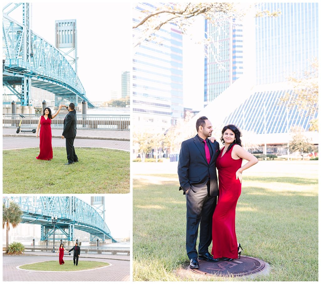 A man twirls his fiancé in a red gown next to a blue bridge.  
