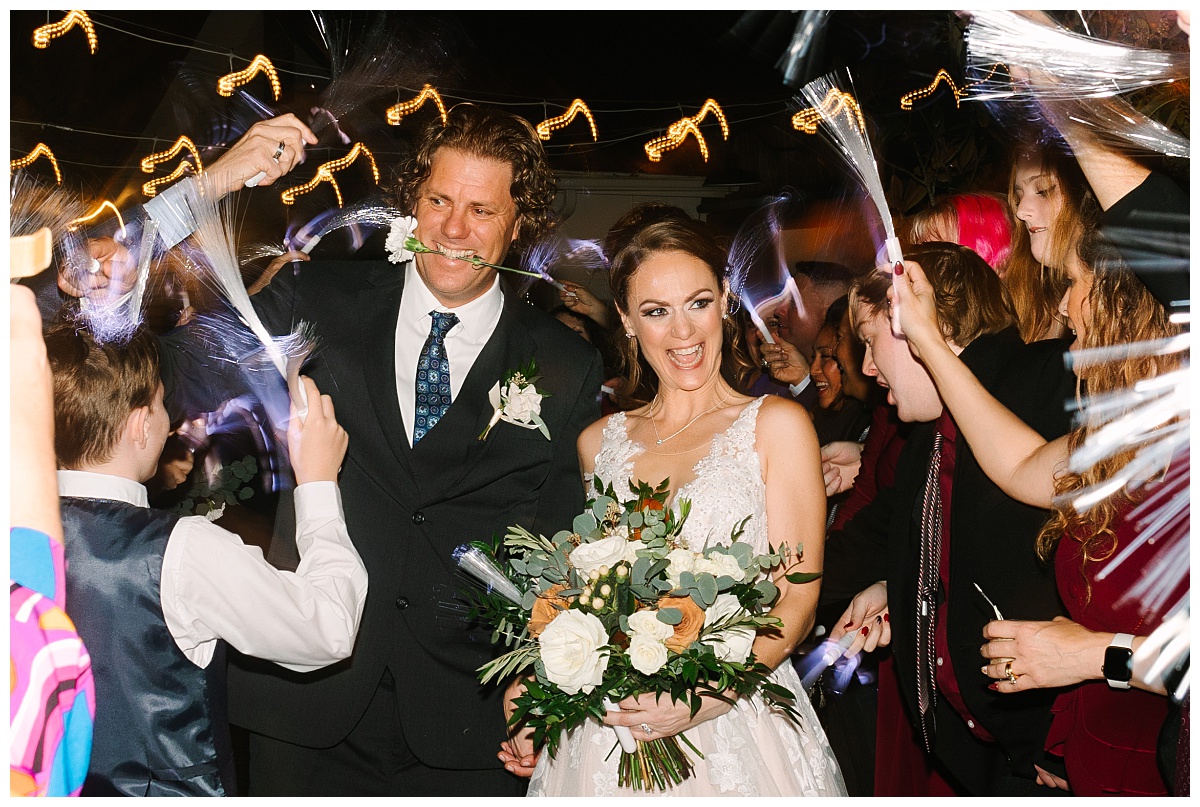 A bride in a white gown and a groom sporting a black tux exit their wedding at The Carriage House surrounded by guests holding sparklers photographed by Laura Perez Photography.