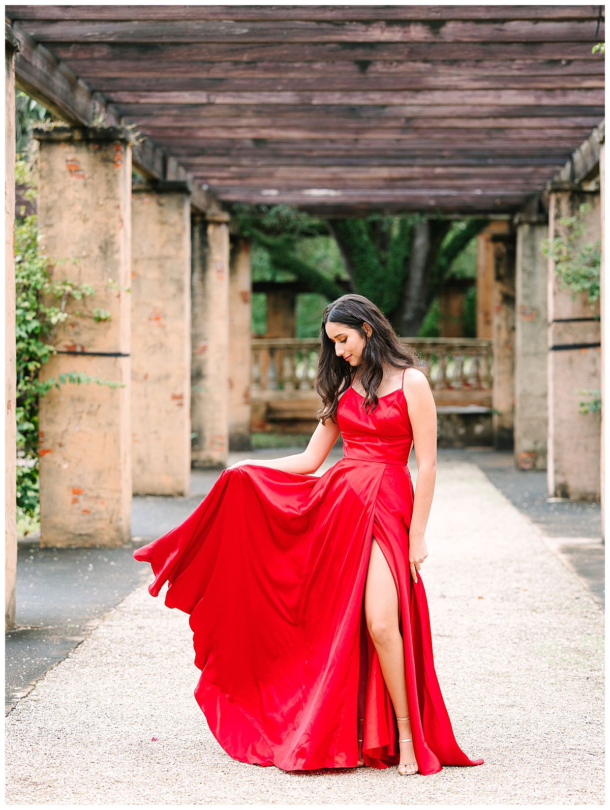 A young woman in a red gown poses in a breezeway similar to Vizcaya Museum in Florida.