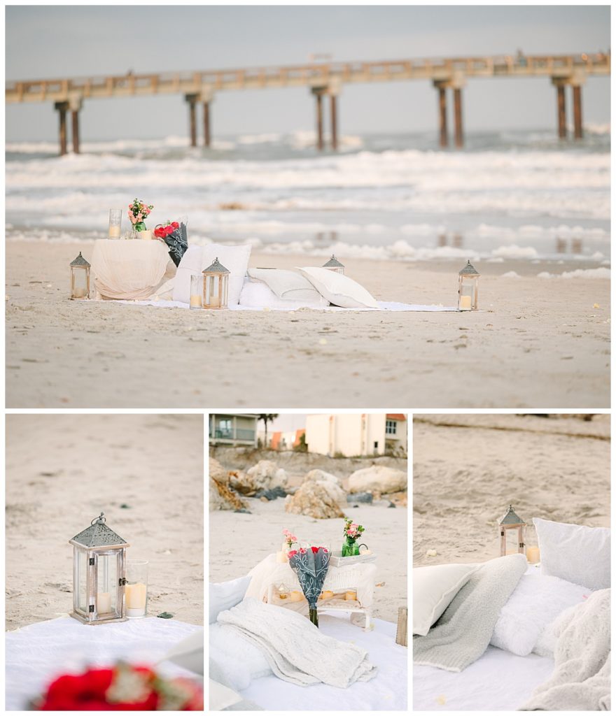 A beach picnic  featuring candle-filled lanterns, fresh flowers, and pillows, set up by Endless Possibilities Event Planning.