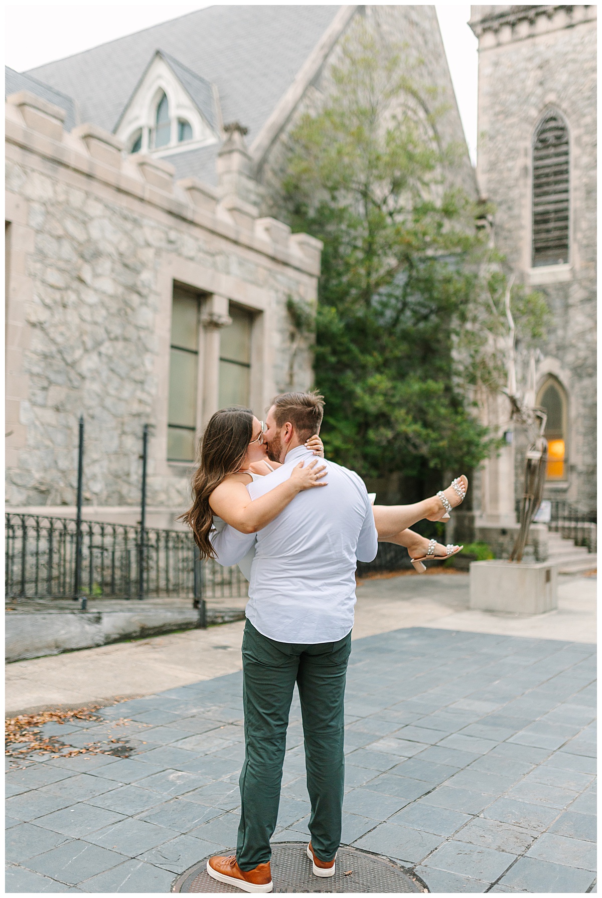 A Florida man wearing jeans and a button up shirt cradles his brunette fiance in his arms for a kiss in front of a stone building in Jacksonville.