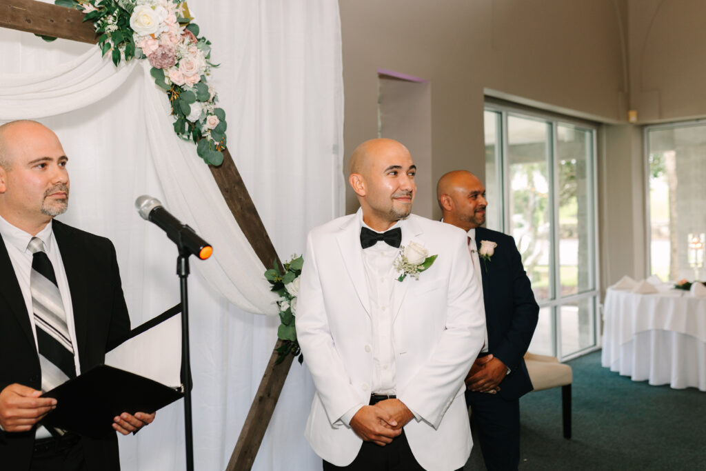 PALM COAST WEDDING AT CHANNEL SIDE GROOM LOOKING AT BRIDE WALK DOWN THE AISLE WITH A SMILE. 