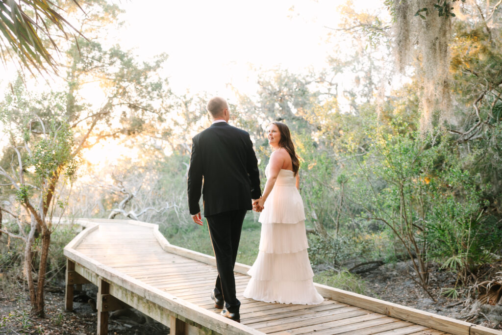 Romantic wedding at Walkers Landing in Amelia Island, Florida, featuring a bride and groom under moss-draped oak trees with a golden sunset reflecting over the water